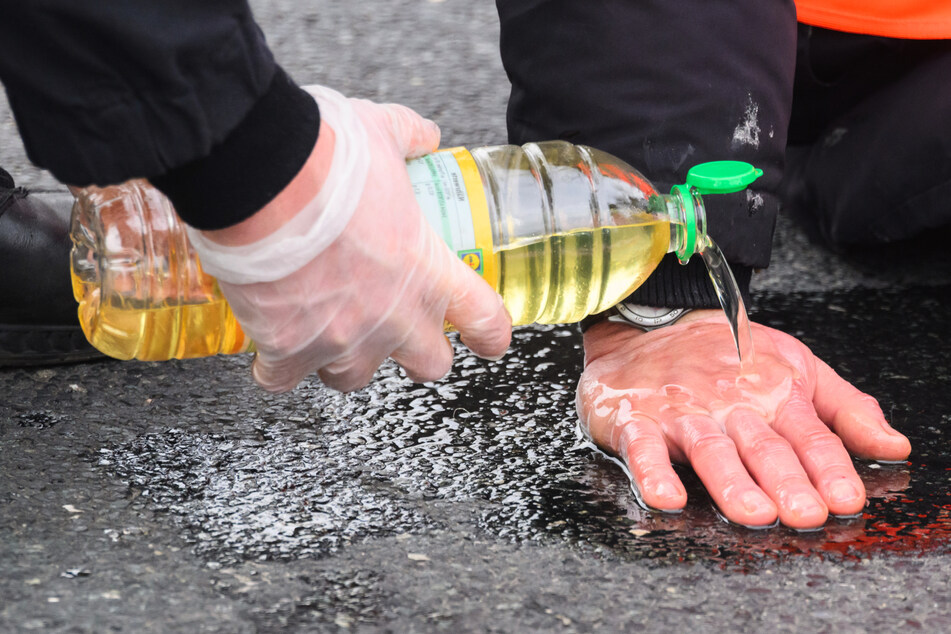 Polizisten versuchen, festgeklebte Hände von Aktivisten der Gruppierung "Letzte Generation" mit Speiseöl von der Straße zu befreien. (Symbolbild)