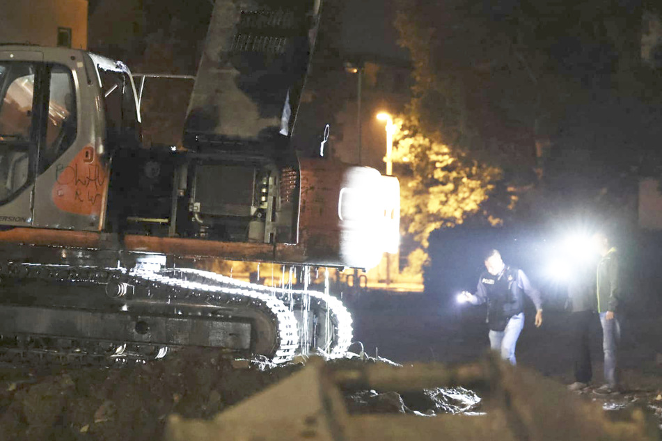 Einsatzkräfte der Polizei suchen am Tatort nach Spuren. Der betroffene Bagger war auf dem Gelände einer Baustelle abgestellt.