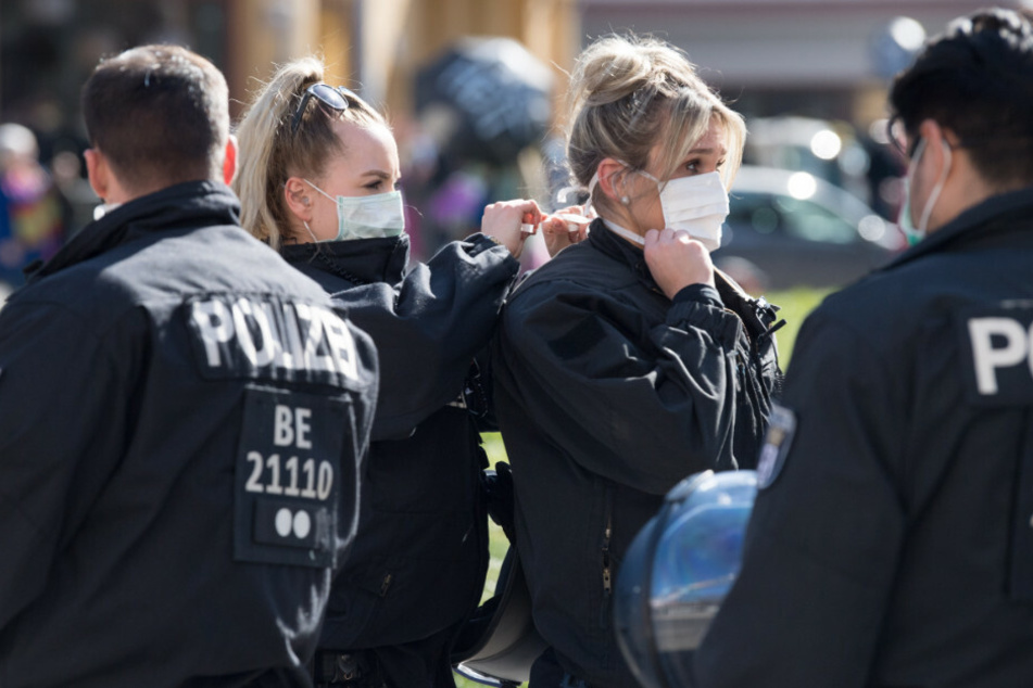 Polizistinnen binden sich bei einer Demonstration unter dem Motto "Grundrechte verteidigen - Sage NEIN zur Diktatur!" auf dem Rosa-Luxemburg-Platz gegenseitig den Mundschutz.