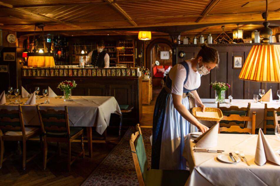 Eine Frau deckt in einem Restaurant einen Tisch ein und trägt Mundschutz.
