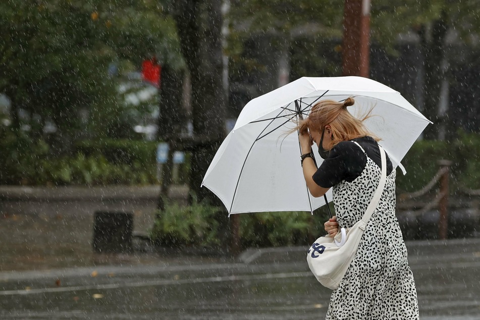 Eine Frau schützt sich mit einem Regenschirm gegen den Wind.