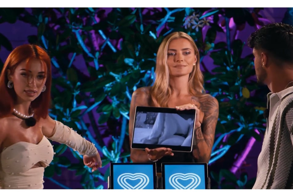 Sophia Thomalla (36, M.) zeigt den anderen Kandidaten den Videobeweis: Dort sind Viki und Kevin im "Boom Boom Room" zu sehen.