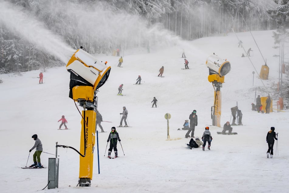 Die Schneekanonen feuern: Wintersportler fahren im Skigebiet Altenberg die Piste hinunter und haben sichtlich Freude.