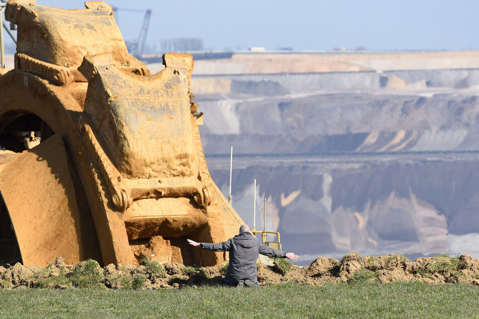 Klimaaktivist Winfried Bernhard kniet an der Tagebaukante bei Lützerath vor einem Braunkohle-Bagger.