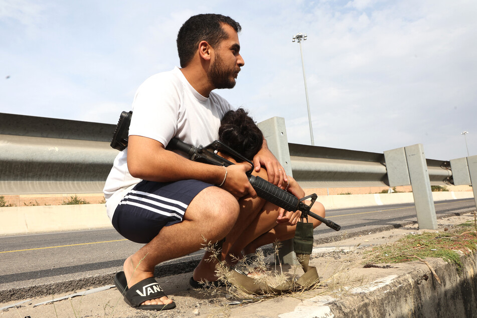Ein bewaffneter Israeli hält seinen Sohn, als sie während eines Raketenangriffs ihr Fahrzeug verlassen, um in Deckung zu gehen.