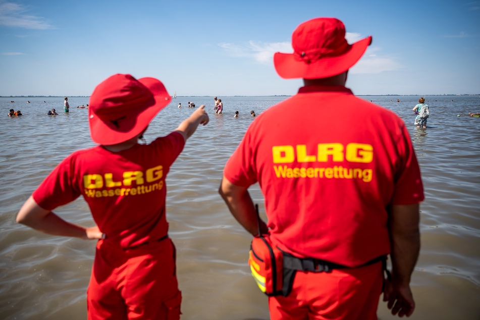 Mitglieder der DLRG (Deutsche-Lebens-Rettungs-Gesellschaft) stehen am Strand.