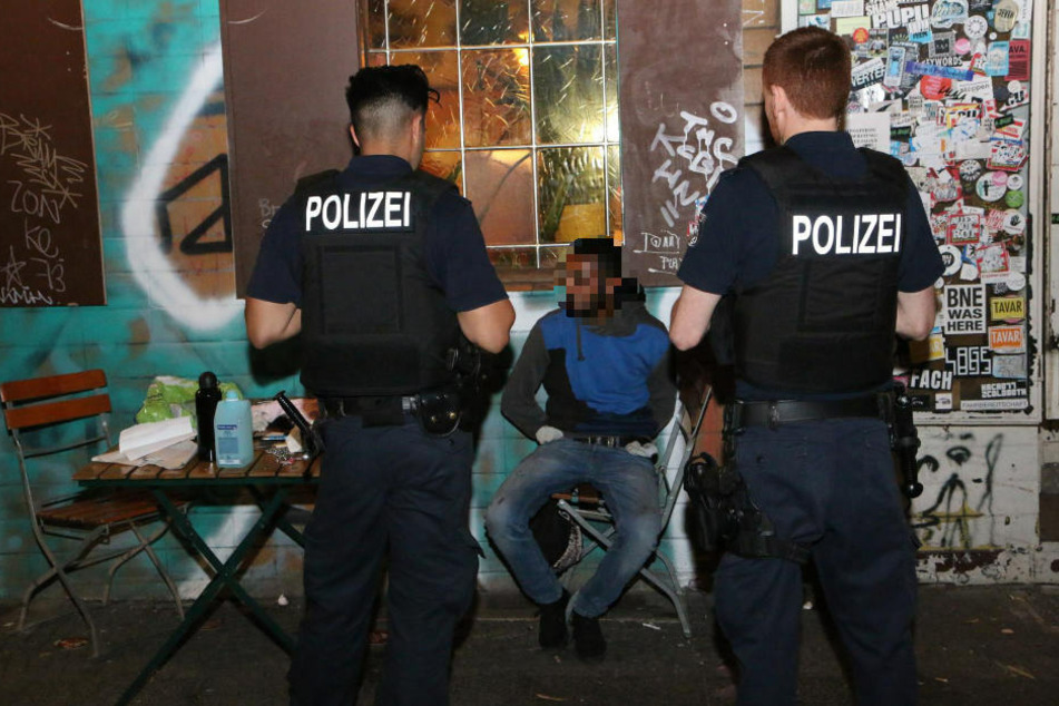 Polizisten bewachen den mutmaßlichen Brandstifter, der gefesselt auf einem Stuhl sitzt.