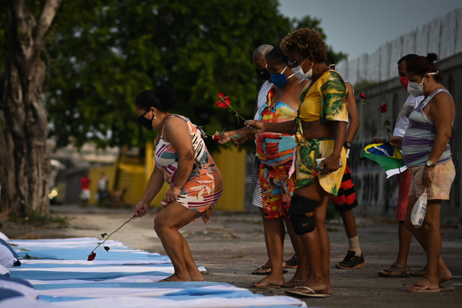 Demonstranten der NGO Rio de Paz halten neben Bahren mit Laken und Kissen Rosen hoch, während eines Protestes im Gedenken an die rund 300.000 Corona-Toten in Brasilien.
