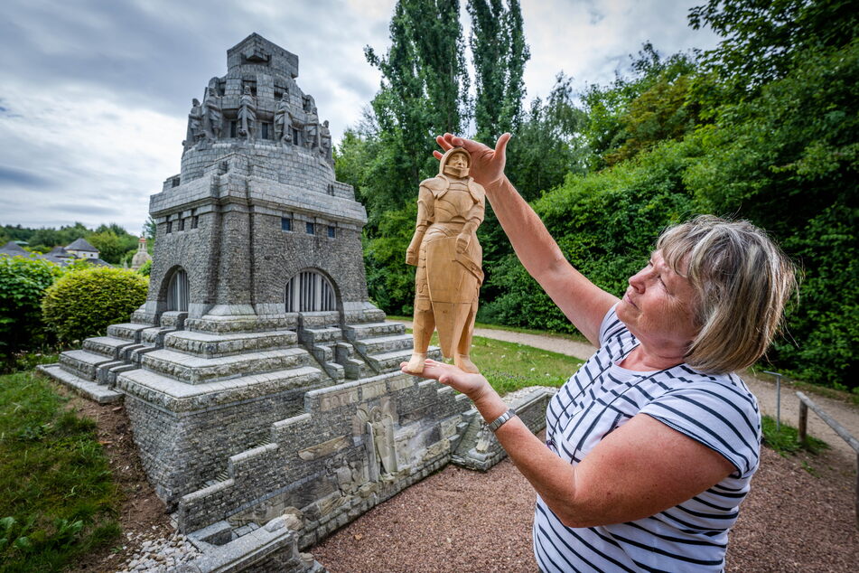 Antje Hempel (63) erklärt die Entstehung des Mini-"Völki". Die geschnitzte Figur aus Lindenholz diente als Vorlage für die gegossene Beton-Replik am Fuß des Mini-Monuments.