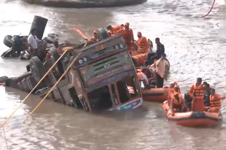 Rettungskräfte versuchen einen Truck aus dem Fluss zu ziehen.