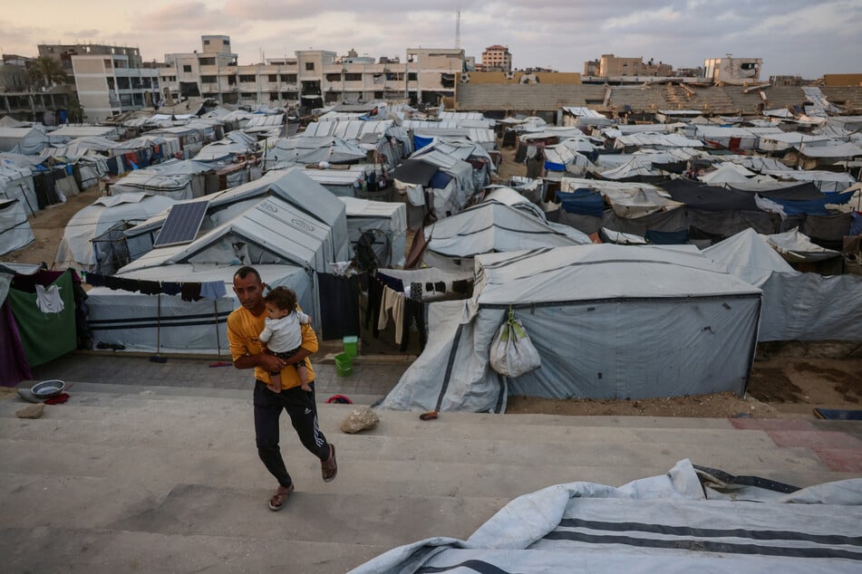 A Palestinian man carries a toddler amid makeshift shelters in Khan Younis in the southern Gaza Strip on May 21, 2026.