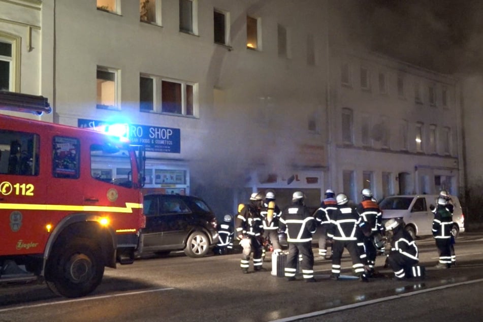 Feuerwehrleute stehen im Stadtteil Wilstorf während des Brandes vor einem Mehrfamilienhaus.