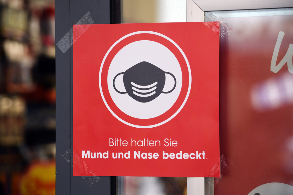 Ein Hinweisschild zum Tragen einer Maske hängt an einer Tür. (Symbolbild)