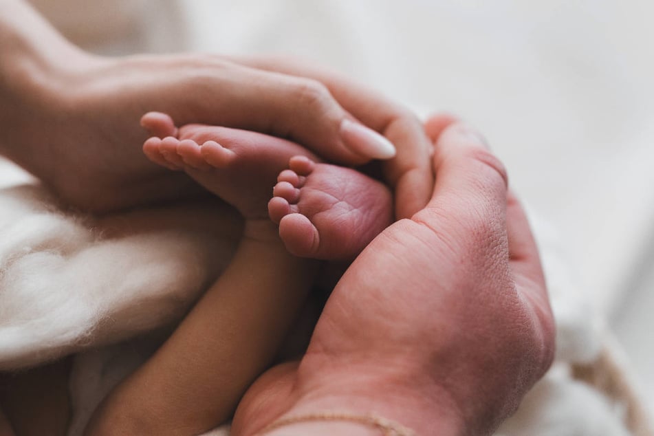 Anne und Gustav umschließen liebevoll die Füße ihres kleinen Sohnes.