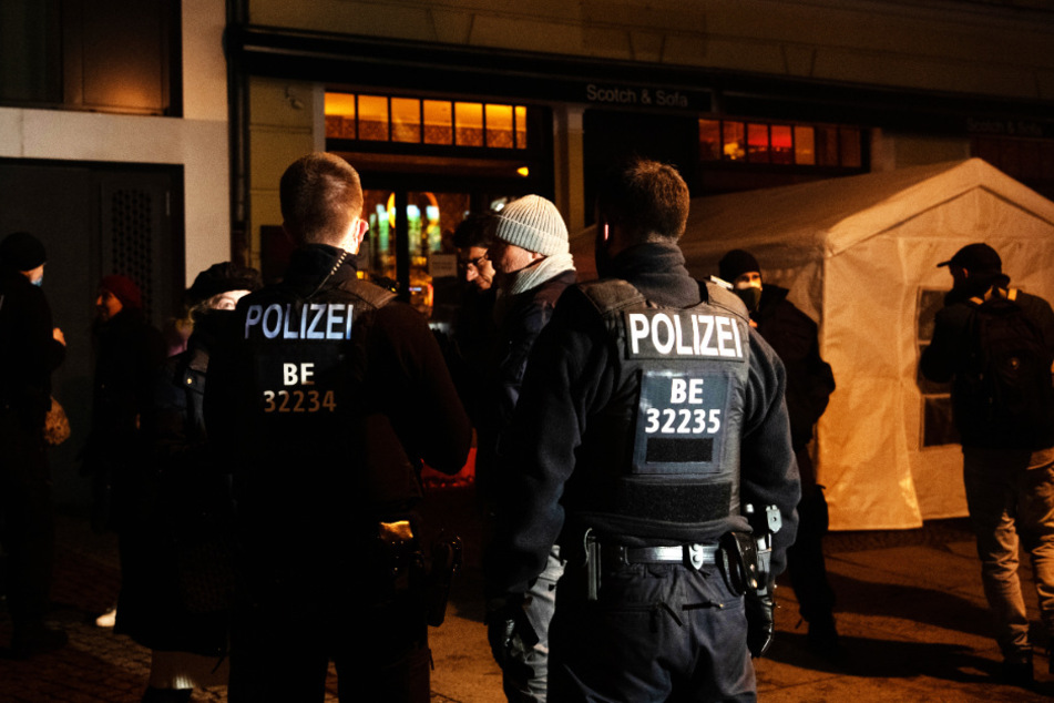 Polizisten und Passanten stehen an der Kollwitzstraße vor einem gastronomischen Betrieb. Wegen des Verstoßes gegen Corona-Regeln war die Berliner Polizei am Donnerstagabend in einem Lokal im Berliner Stadtteil Prenzlauer Berg im Einsatz.
