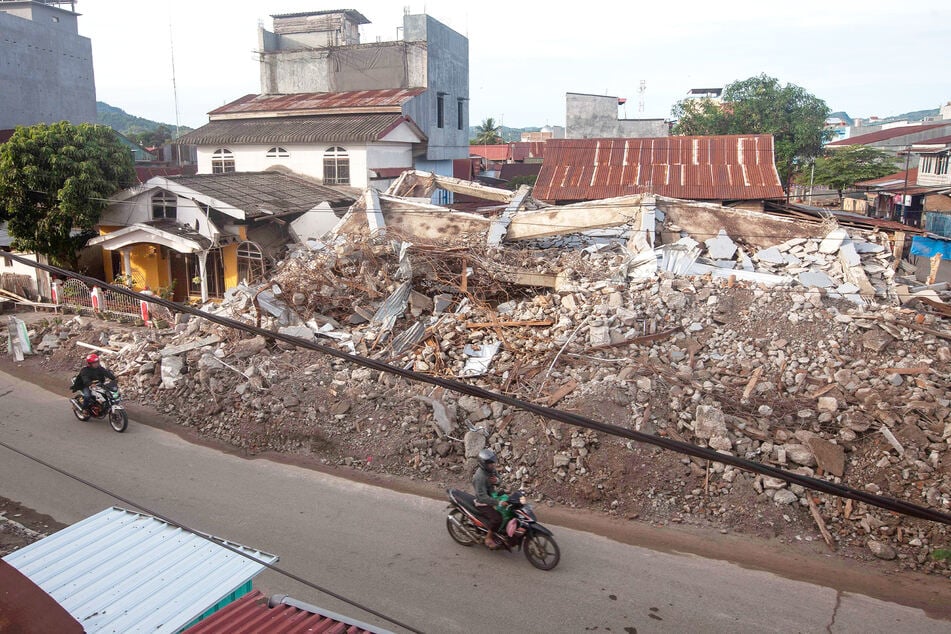 Pengendara sepeda motor berjalan melewati gedung-gedung yang roboh akibat gempa bumi.