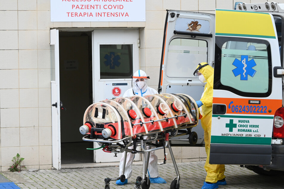 Mitarbeiter in Schutzkleidung stehen vor einem Krankenhaus in Italien - die Zahl der Corona-Toten steigt in dem südeuropäischen Land wieder an.