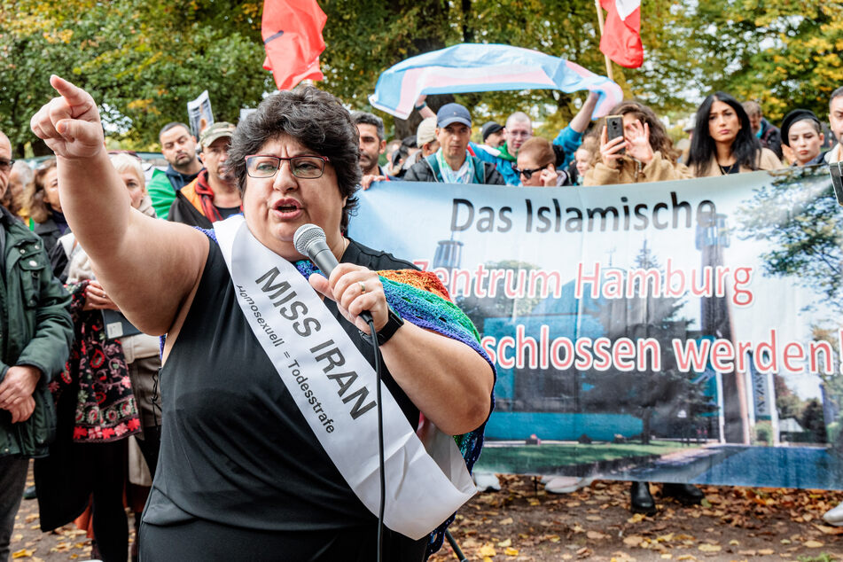 Eine iranische Queer-Aktivistin spricht vor einem Transparent mit der Aufschrift "Das Islamische Zentrum Hamburg muss geschlossen werden".