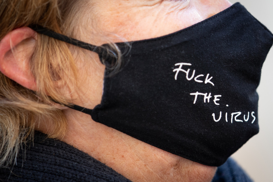 "Fuck The Virus" steht auf der schwarzen Mund-Nase-Bedeckung einer Frau.