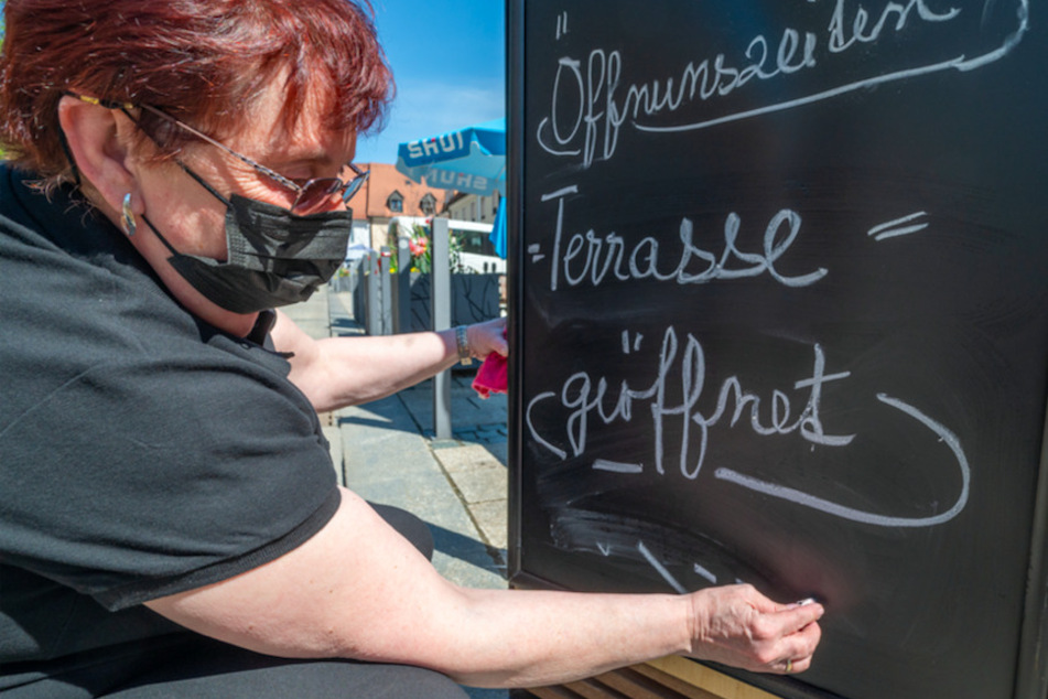 Eine Frau schreibt "Terrasse = geöffnet" vor einem Café in Tirschenreuth auf eine Hinweistafel.