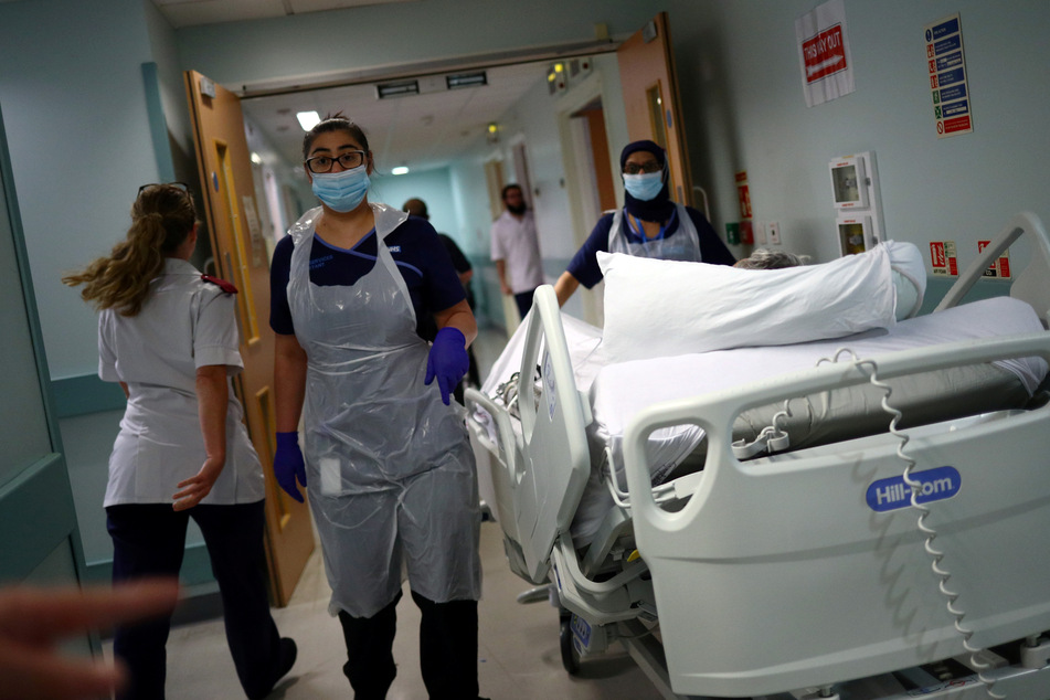 Medizinische Mitarbeiter des Royal Blackburn Lehrkrankenhaus in Schutzkleidung schieben einen Patienten auf einem Krankenhausbett durch einen Korridor.