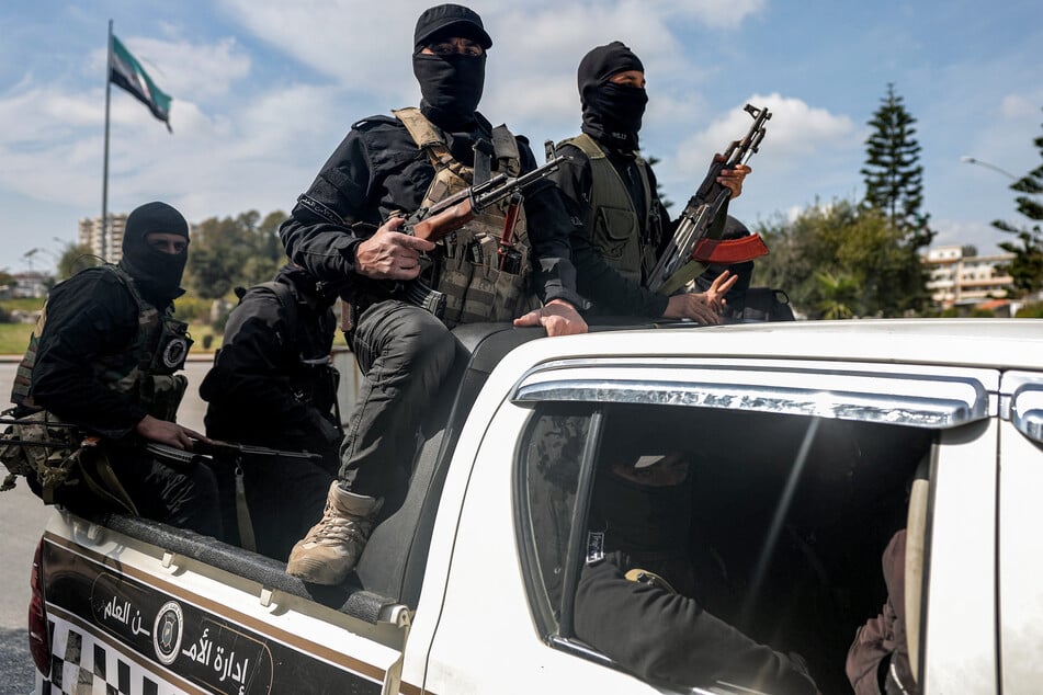 Security forces loyal to the interim Syrian government ride in the back of a vehicle moving along a road in Syria's western city of Latakia on Sunday.