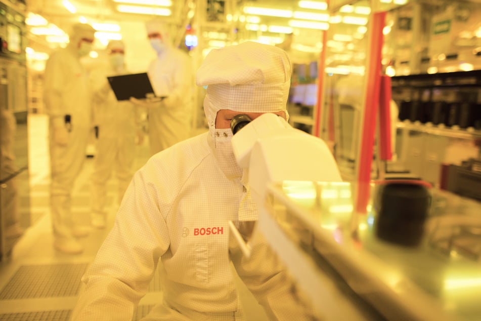 In einem Gelbraum in Reutlingen kontrolliert ein Bosch-Mitarbeiter eine Halbleiterscheibe mit einem Mikroskop auf mögliche Fehler.