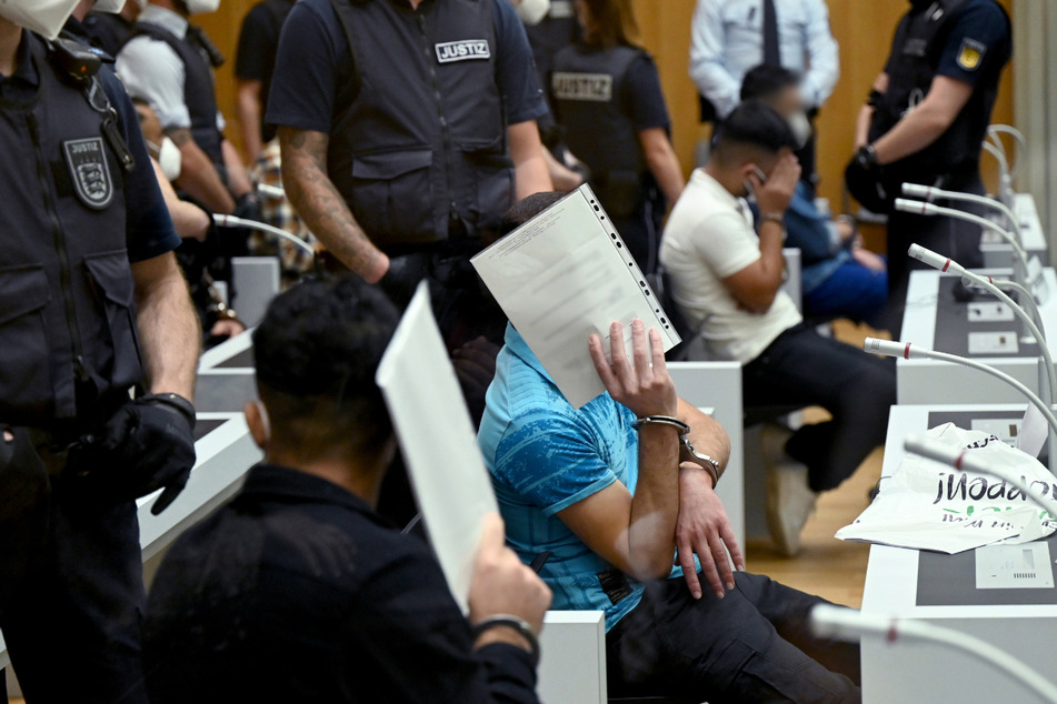 Die Angeklagten schützen vor Prozessbeginn ihre Gesichter mit Aktenordnern.
