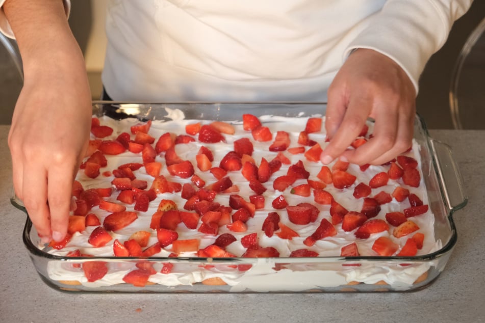 Bei der Zubereitung von Erdbeer-Tiramisu werden Löffelbiskuits, Mascarpone und Erdbeeren abwechselnd in eine große Form geschichtet.