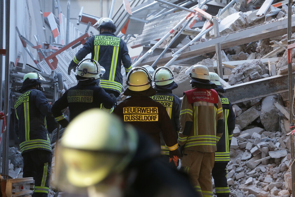 Feuerwehrleute stehen in einer Hauseinfahrt vor Bauschutt.