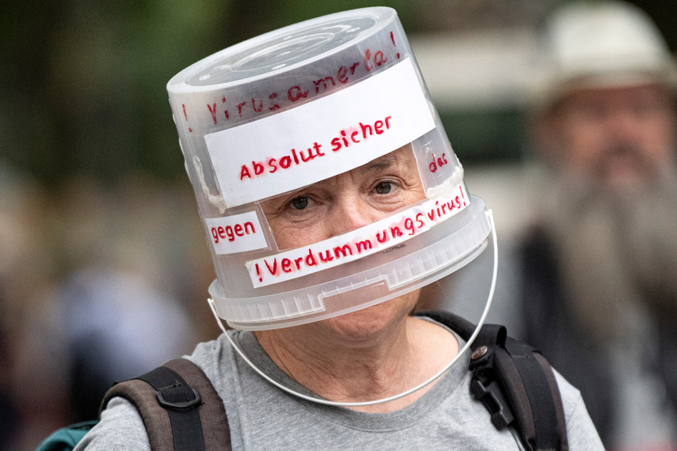 Ein Demonstrant läuft mit einem auf den Kopf gesetzten Plastikeimer, beschriftet mit "Absolut sicher gegen das Verdummungsvirus", durch Berlin-Charlottenburg.