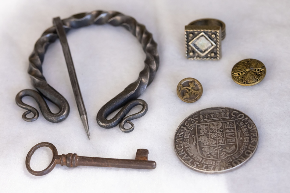 Kleine Schätze aus dem Mittelalter wie eine Gewandspange, eine Münze und Knöpfe.
