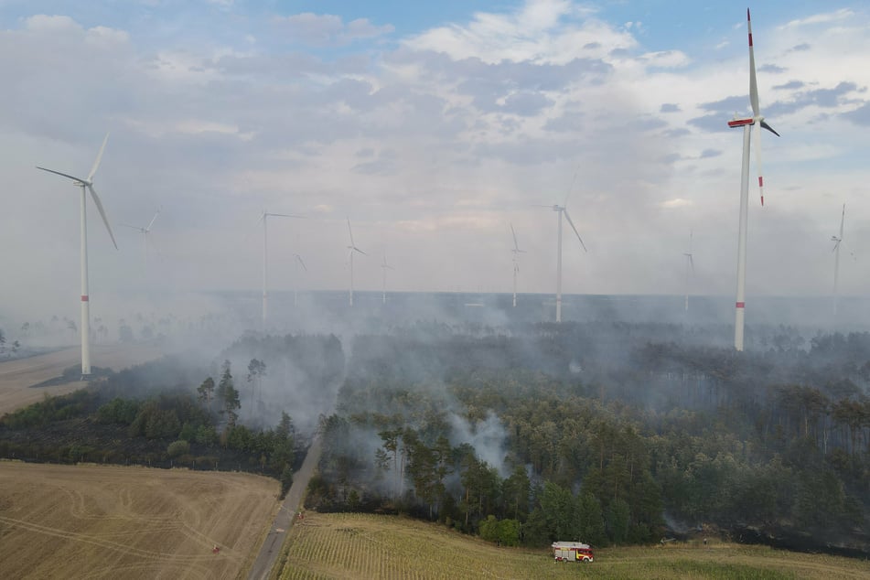 Es brennt im Wald zwischen Windrädern, mindestens eine Anlage steht innerhalb der Brandfläche, andere Windkraftanlagen sind gefährdet.