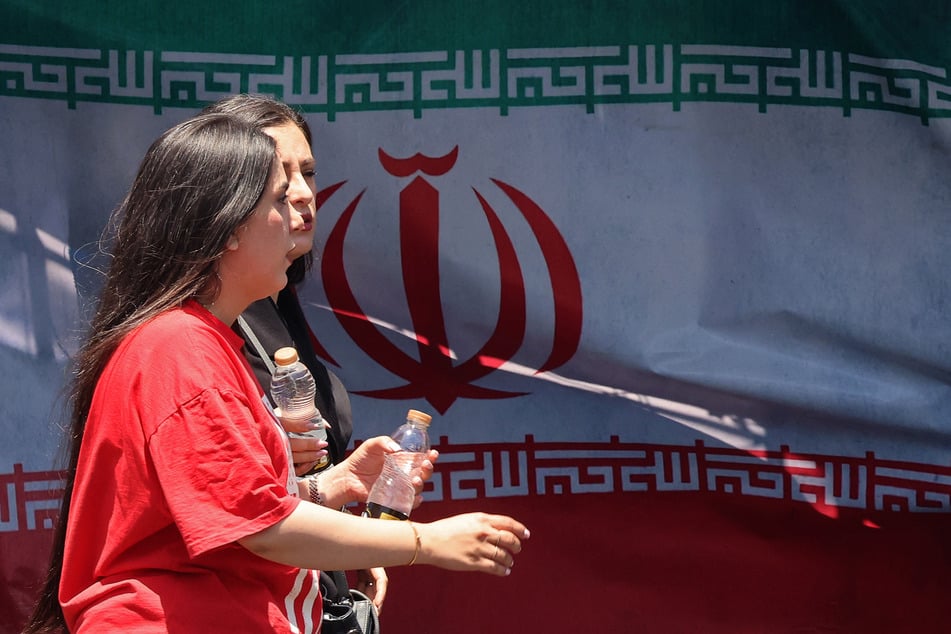 Women walk past Iran's national flag at the Vanak Square in Tehran on June 10, 2026.