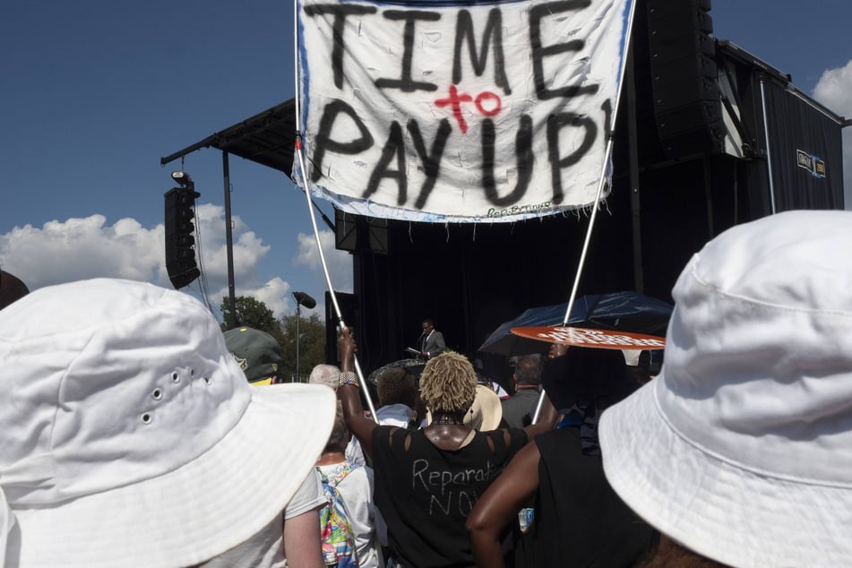 A participant at the 60th anniversary March on Washington raises a sign reading "Time to Pay Up" demanding reparations.