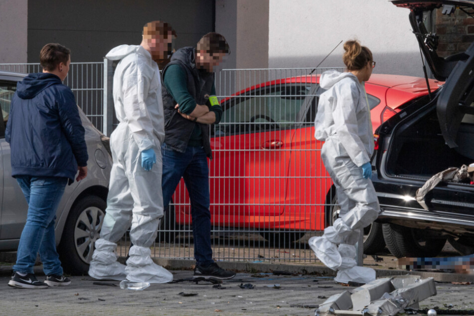 Mitarbeiter der Spurensicherung stehen in Limburg an dem Wrack eines dunklen Autos, unter dem die Leiche einer Frau liegt.