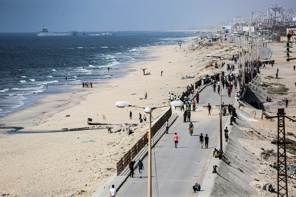 A ship transporting international humanitarian aid is moored at the US-built Trident Pier as Palestinians walk along a main road near Nuseirat in the central Gaza Strip on May 21, 2024.