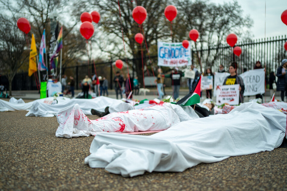 Demonstrators draped in white cloths lie on the ground in a "die in" outside the White House to protest US government support for Israel's genocide.