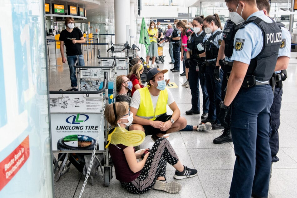 Polizisten unterhalten sich mit den Aktivisten, die sich am Flughafen München mit Gepäckwagen in einem Durchgangsbereich zu den Abfluggates aneinander gekettet haben.