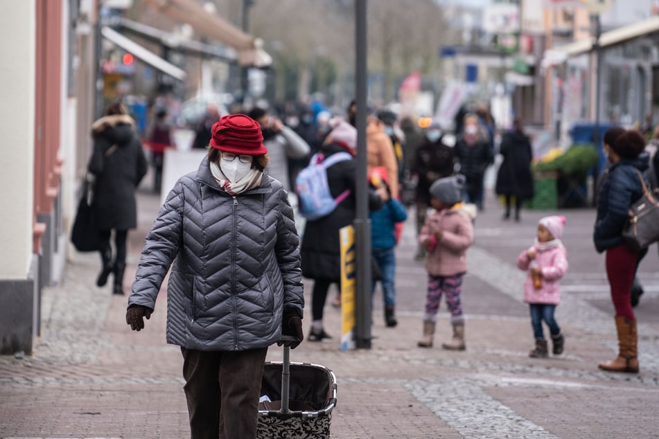 Eine Frau (l) geht mit einer FFP2-Maske geschützt durch die Fußgängerzone der Stadt Oberursel.