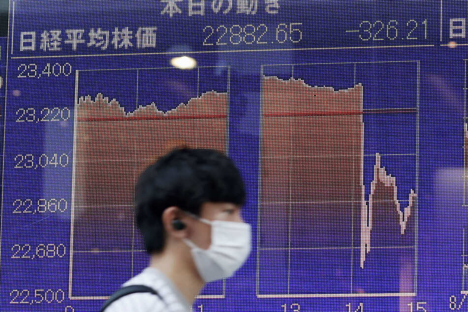 Ein Passant trägt einen Mundschutz und geht an einer elektronischen Anzeigetafel vorbei, die den Aktienindex Nikkei 225 zeigt.