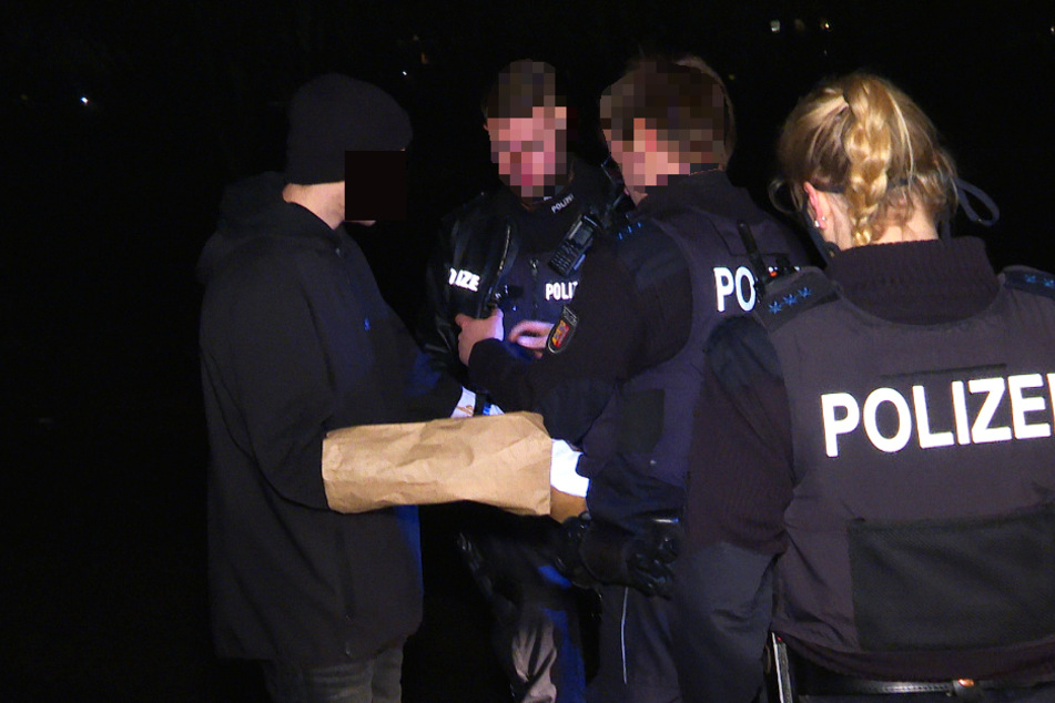 Die Polizisten packen die Hände eines Jugendlichen in Papiertüten ein, um etwaige Schmauchspuren zu sichern.