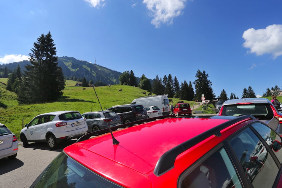 Autos von Ausflüglern stehen auf dem voll belegten Parkplatz der Alpe Kammeregg im strahlenden Sonnenschein. Viele Gemeinden haben nun mit hohen Parkgebühren auf die Flut an Touristen reagiert.