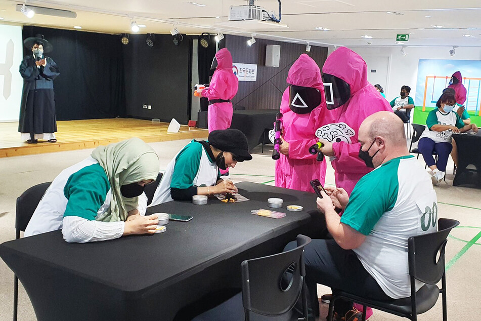 Das Foto zeigt, wie in den VAE "Squid Game" nachgespielt wurde. Hier versuchen drei Teilnehmer, ihre Figuren aus einem Zuckerkeks zu lösen, ohne, dass diese zerbricht.