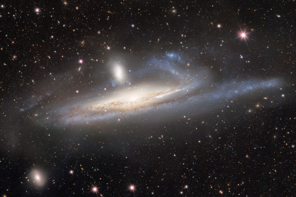 Ein kosmisches Tauziehen: Spiralgalaxie (erkennbar an den geschwungenen Armen) gegen Zwerggalaxie (Mitte oben).