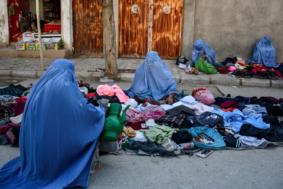 Afghan burqa-clad women sell used clothes along a street in Maymana, the capital of Afghanistan's northwestern Faryab province, on January 13, 2025.