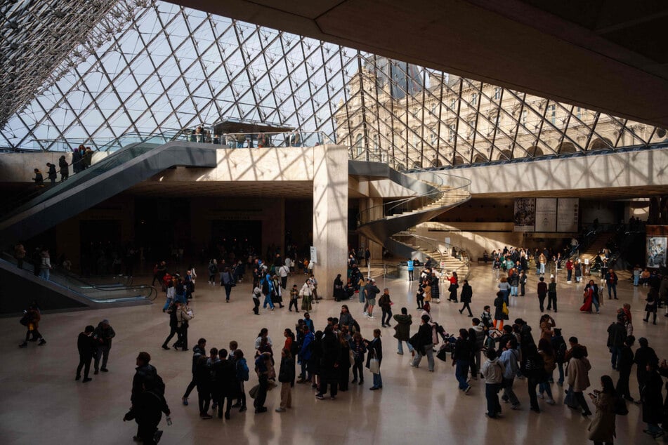 Visitors walk under the famous Louvre glass pyramid.