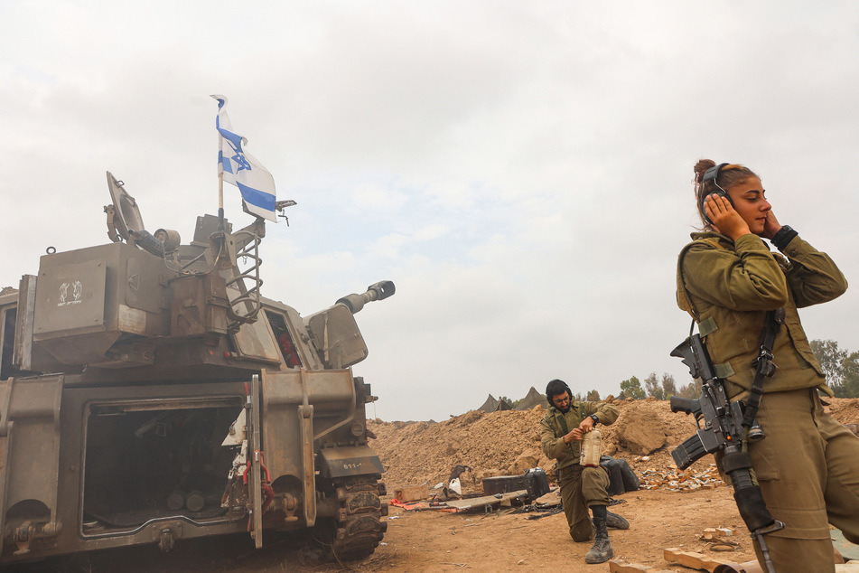 Eine IDF-Soldatin hält sich die Ohren zu, während israelische Artillerie feuert.