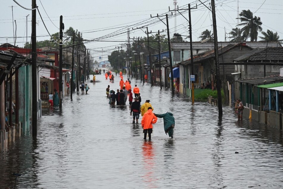 People walk through a flooded street in Batabano, Mayabeque province, Cuba on August 29, 2023, during the passage of tropical storm Idalia.