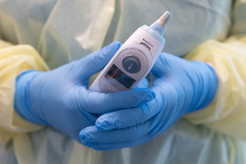 Eine medizinische Angestellte hält ein Fieberthermometer in der Hand.
